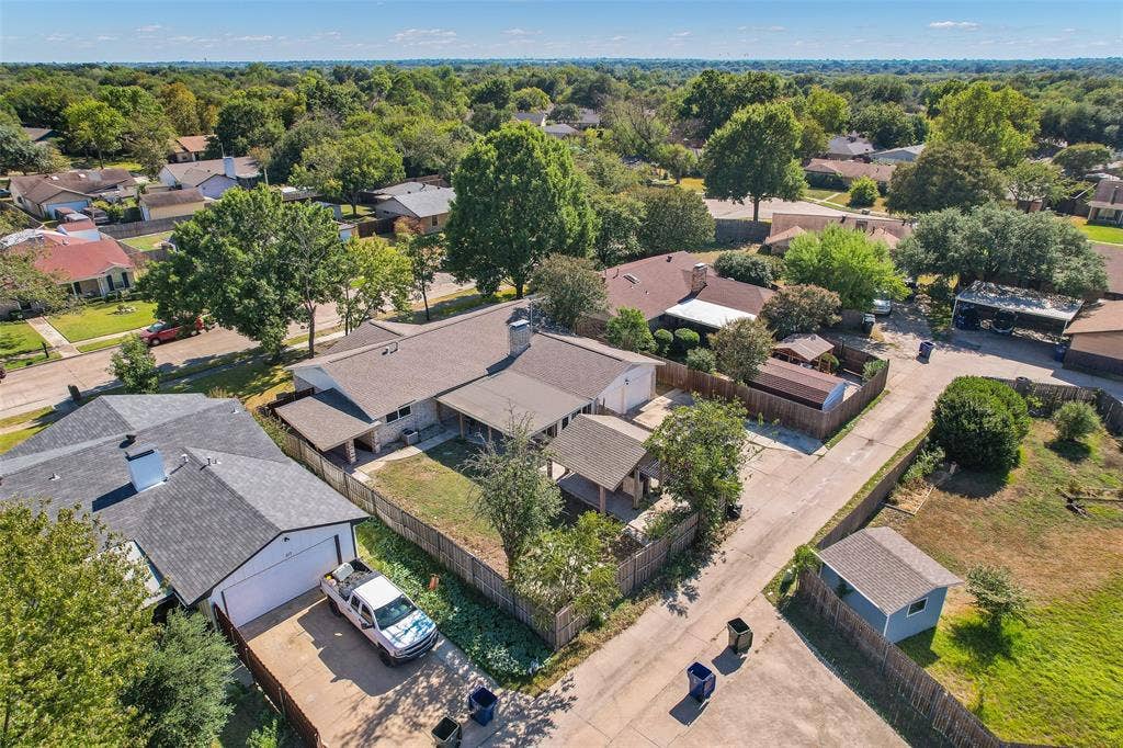 Aerial perspective highlighting the property with a two-car garage, fenced backyard, and surrounding mature trees