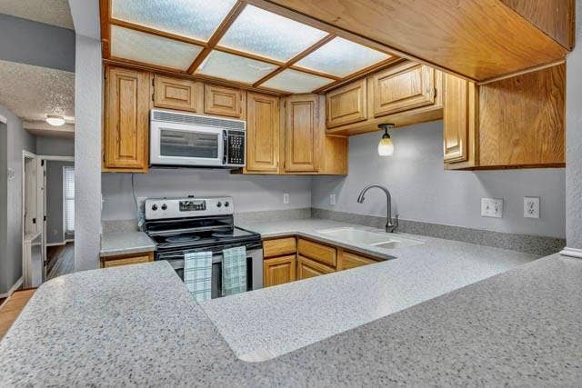 2503 Shady Ridge Drive, Bedford, TX 76021 Kitchen featuring light-tone wood cabinetry, solid-surface countertops, dual-basin sink with pull-down faucet, integrated overhead grid lighting, and stainless steel microwave and range appliances