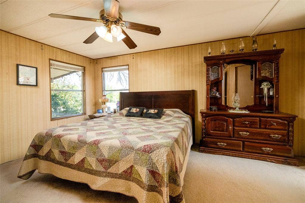 Interior room featuring wood-panel wall finishes, neutral carpeting, and a multi-blade ceiling fan with integrated light fixture
