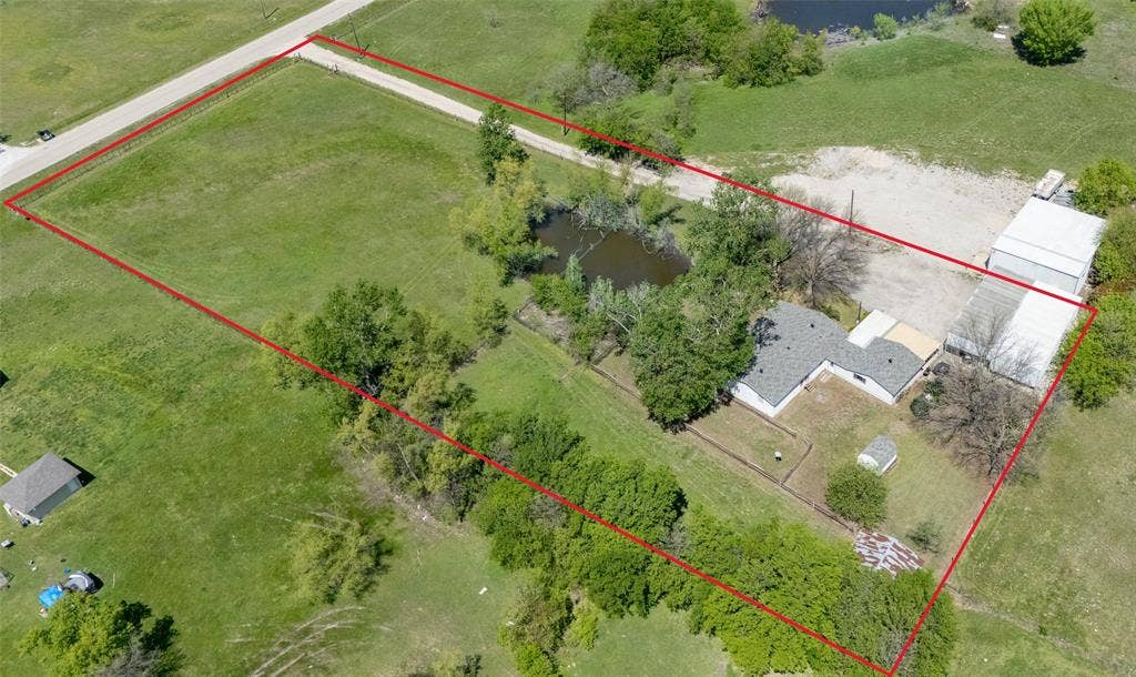 Expansive acreage featuring a private pond, mature tree canopy, multiple detached structures, and extensive open green space