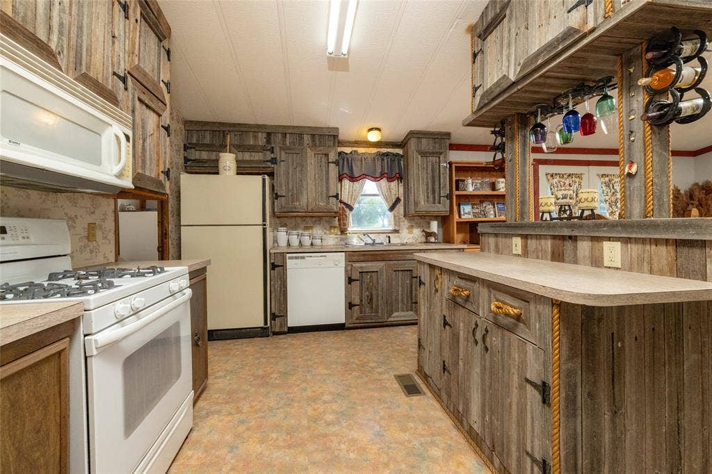 Kitchen featuring custom distressed wood cabinetry, built-in overhead wine rack, dual-basin sink, gas range, and integrated dishwasher