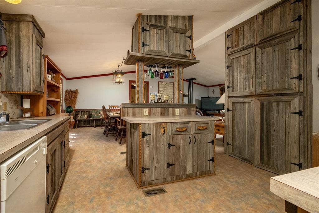 Kitchen featuring reclaimed wood cabinetry, a central island with an overhead glass rack, integrated countertop, and hardware accents