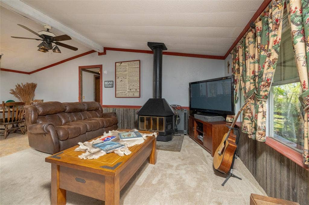Living area featuring a black metal freestanding fireplace, paneled wainscoting, and a ceiling fan with integrated lighting