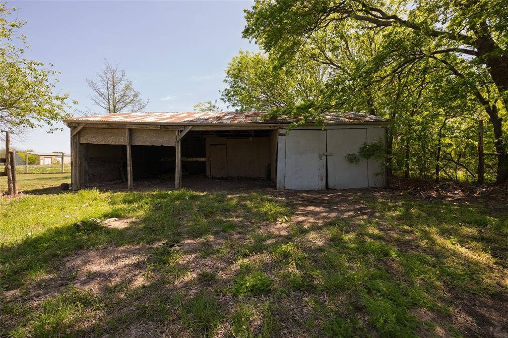 Outbuilding featuring a metal roof, open-bay storage, and enclosed storage area set on a parcel with mature trees