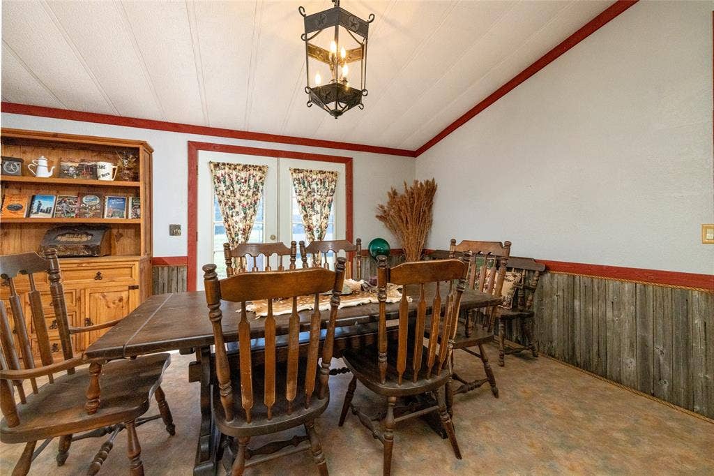 Dining space featuring wood-paneled wainscoting, built-in wooden cabinetry, a vaulted ceiling, a wrought-iron multi-light pendant fixture, and double glass-panel doors