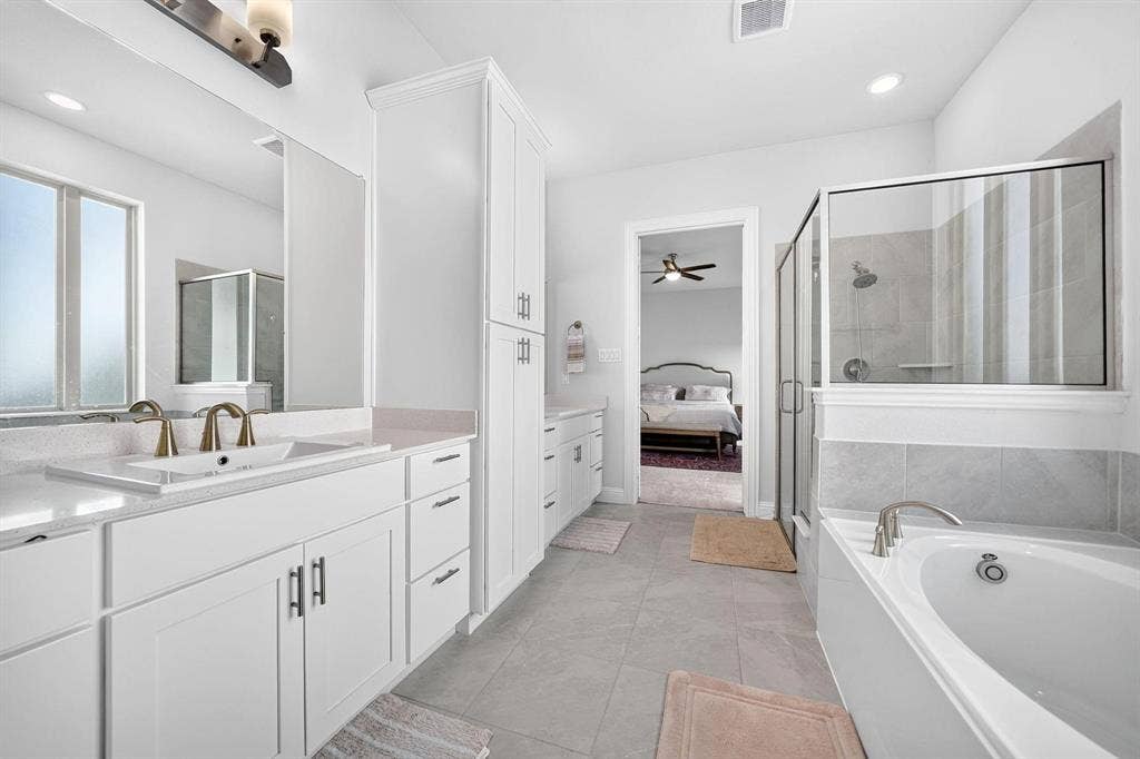 Bathroom featuring a white double vanity with stone countertops, a glass-enclosed shower, a deep soaking tub, and a tall linen storage cabinet