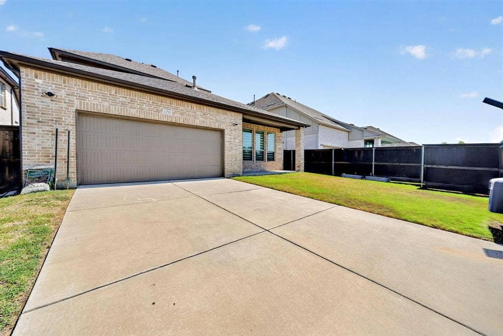 Brick exterior featuring a multi-car garage, concrete driveway, and a fenced lawn area