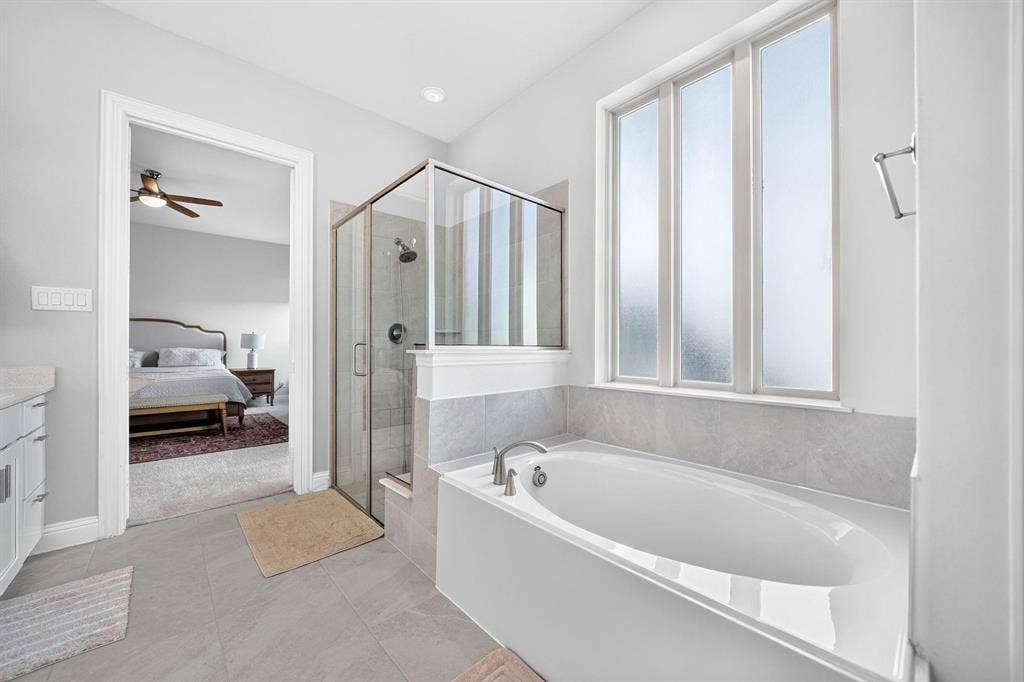 Bathroom featuring a soaking tub with a tiled surround, a separate glass-enclosed shower, large-format tile flooring, and frosted pane windows