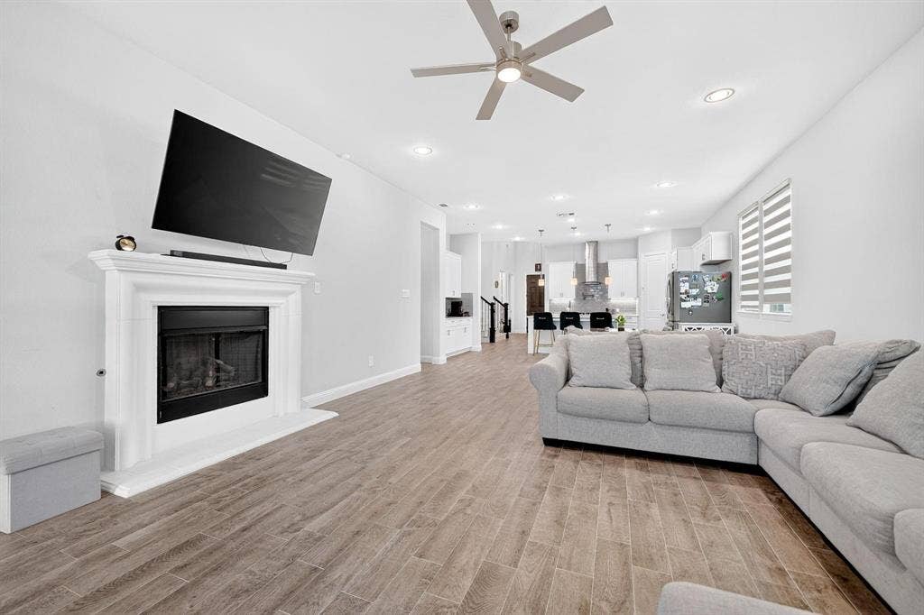 Open-concept interior featuring wood-finish tile flooring, recessed lighting, a ceiling fan, and a fireplace with a decorative mantel