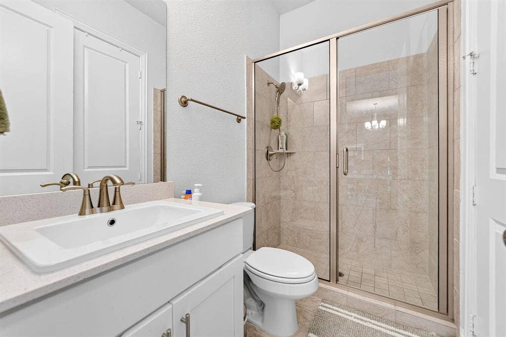 Bathroom featuring a vanity with a light-toned countertop, drop-in sink, metallic fixtures, and a glass-enclosed shower with tile surround