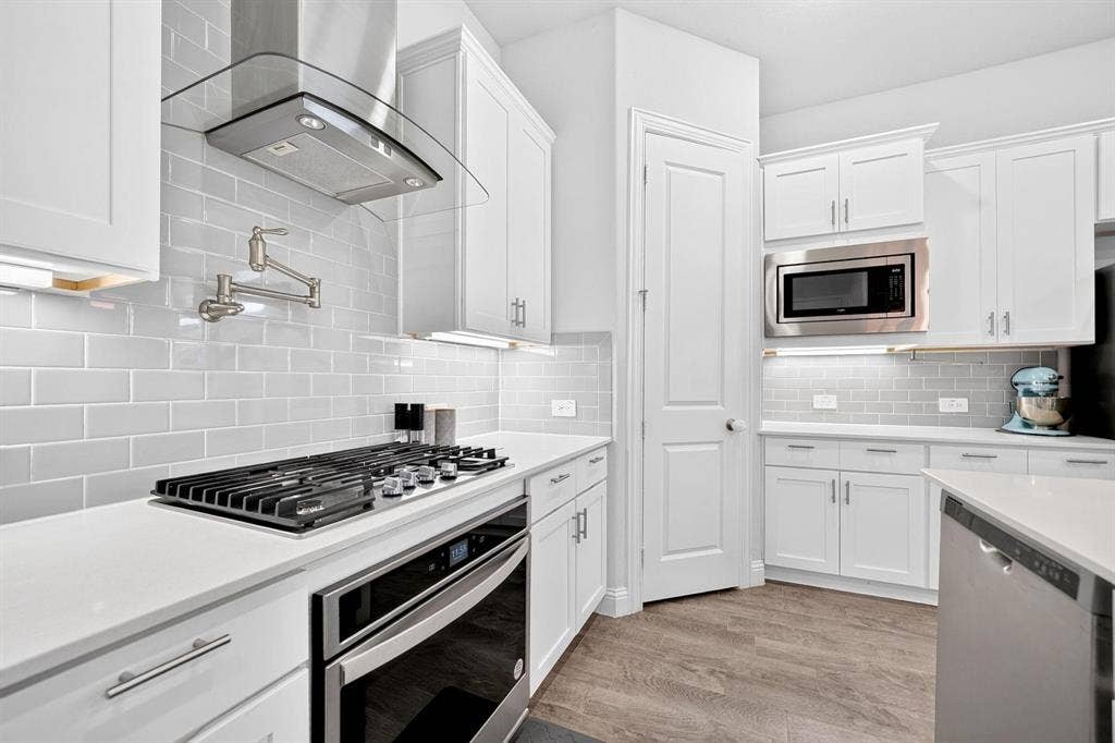 Kitchen featuring white shaker-style cabinetry, quartz countertops, subway tile backsplash, stainless steel gas cooktop with wall-mounted pot filler, and wood-finish flooring