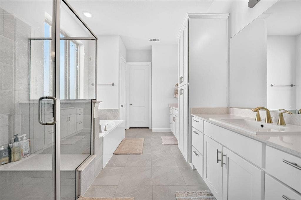 Bathroom featuring a glass-enclosed shower with tile surround, white cabinetry, integrated stone-finish countertops, built-in floor-to-ceiling storage, and a deep soaking tub
