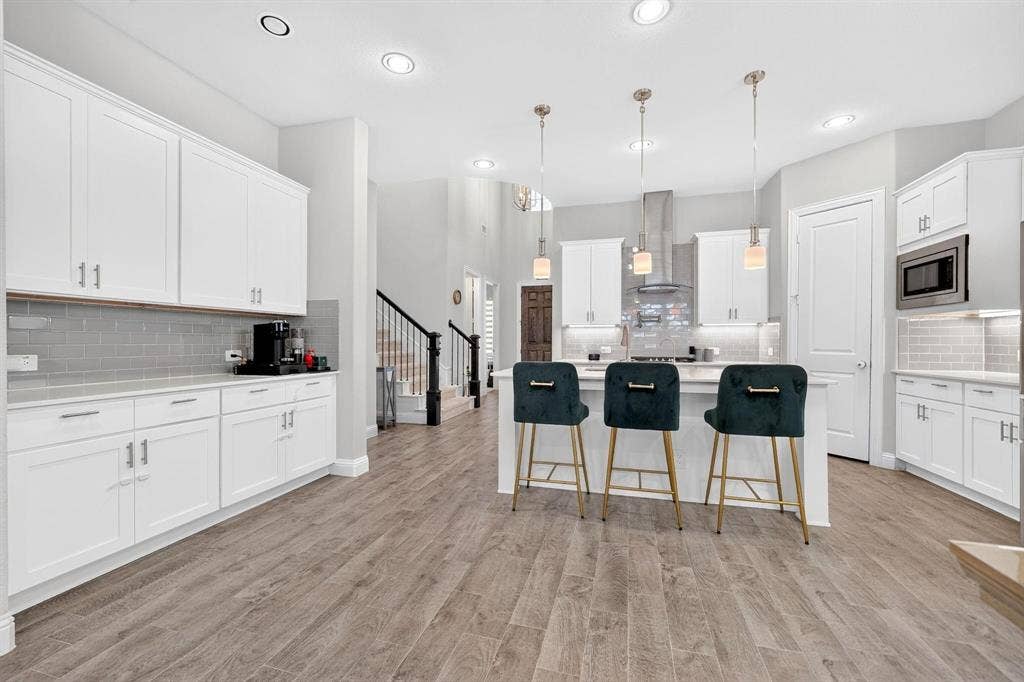 Kitchen featuring white shaker-style cabinetry, wood-finish flooring, subway tile backsplash, a central island with quartz countertop, and stainless steel hood range