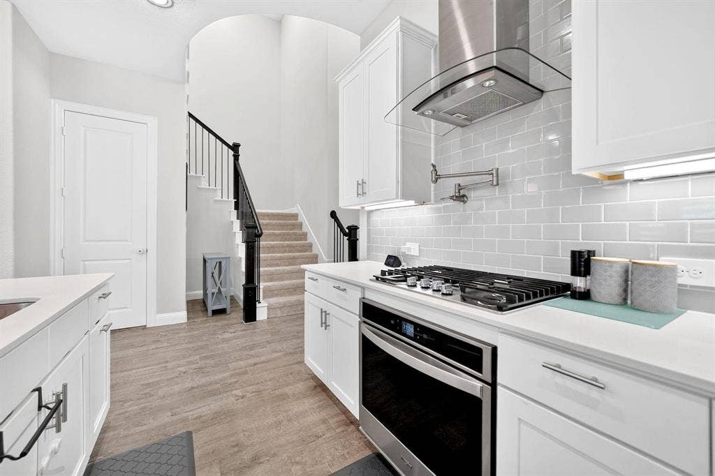 Kitchen featuring white shaker-style cabinetry, solid-surface countertops, subway tile backsplash, stainless steel gas range with wall-mounted pot filler, and stainless steel range hood