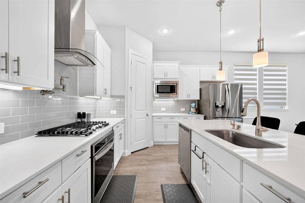 Kitchen featuring white shaker-style cabinetry, quartz countertops, subway tile backsplash, stainless steel appliances including a gas range with a pot filler, and a center island with an undermount sink