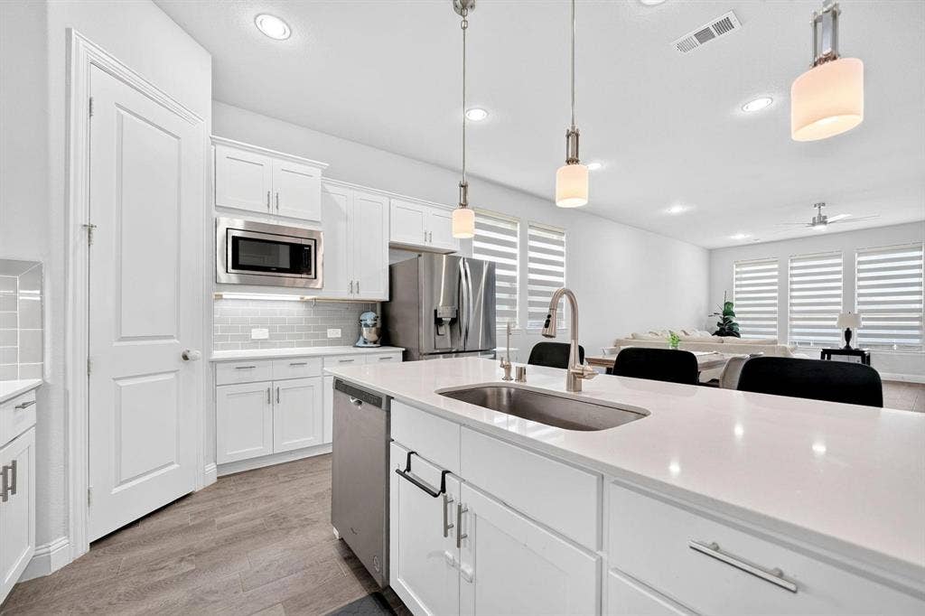 Kitchen featuring a central island with a quartz countertop, stainless steel appliances, shaker-style cabinetry, tiled backsplash, and wood-finish flooring