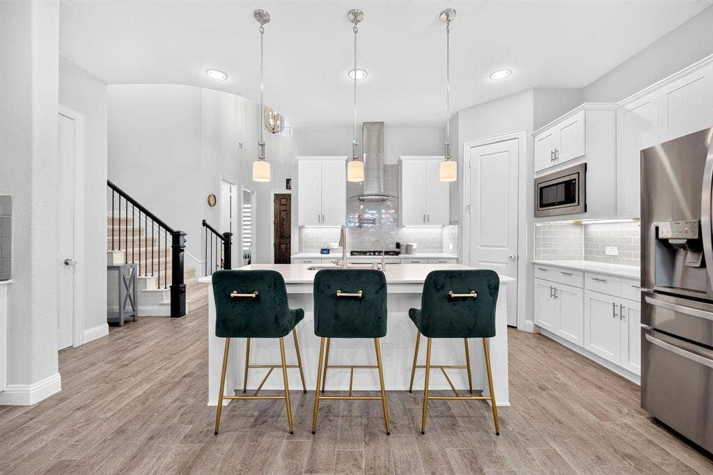 Kitchen featuring white cabinetry, quartz countertops, a central island with undermount sink, stainless steel appliances, and wood-finish flooring