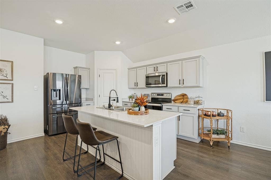 1506 Buckaroo Lane, Josephine, TX 75189 Kitchen featuring light grey shaker-style cabinetry, quartz countertops, a central island with an integrated sink, stainless steel appliances, and wood-finish flooring