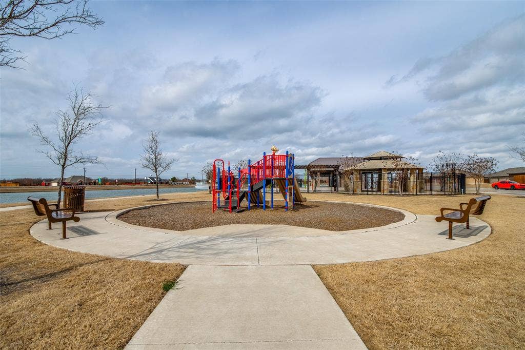 1506 Buckaroo Lane, Josephine, TX 75189 Community recreational area featuring a central playground structure with mulch ground cover, concrete perimeter pathways, integrated park benches, and a stone-clad pavilion