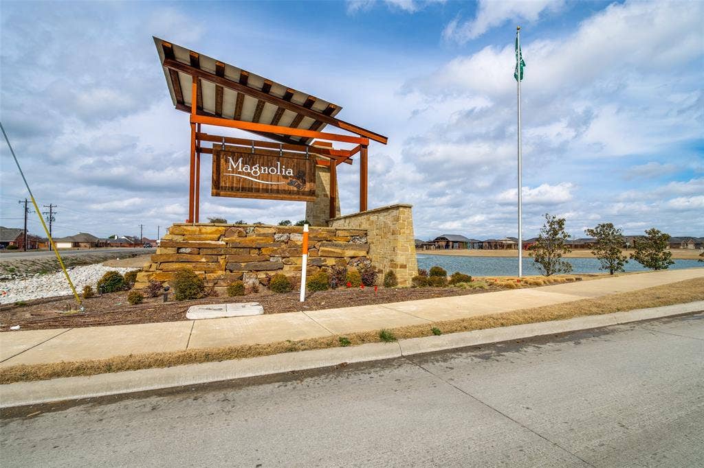 1506 Buckaroo Lane, Josephine, TX 75189 Community entrance featuring a metal and stone structural monument, concrete sidewalk, pond, and flagpole