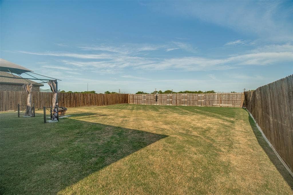 1506 Buckaroo Lane, Josephine, TX 75189 Expansive backyard featuring a level lawn, full-perimeter wood privacy fencing, and a metal-frame shade structure