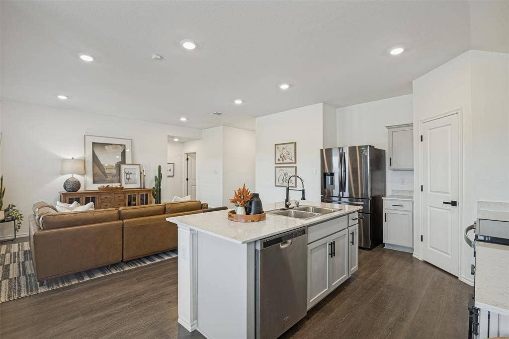 1506 Buckaroo Lane, Josephine, TX 75189 Kitchen featuring a central island with a stone-surface countertop, stainless steel dishwasher, dual-basin undermount sink, and matte black hardware, accented by wood-finish flooring and recessed lighting