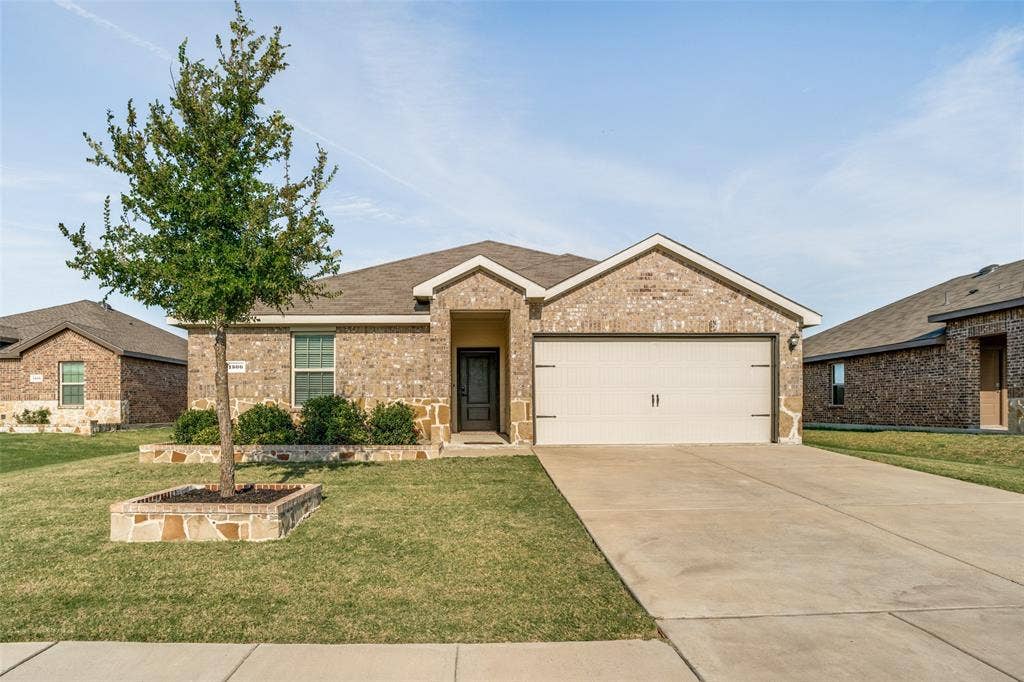 1506 Buckaroo Lane, Josephine, TX 75189 Single-story brick exterior featuring a recessed entryway, attached two-car garage, concrete driveway, and stone-accented landscape bed