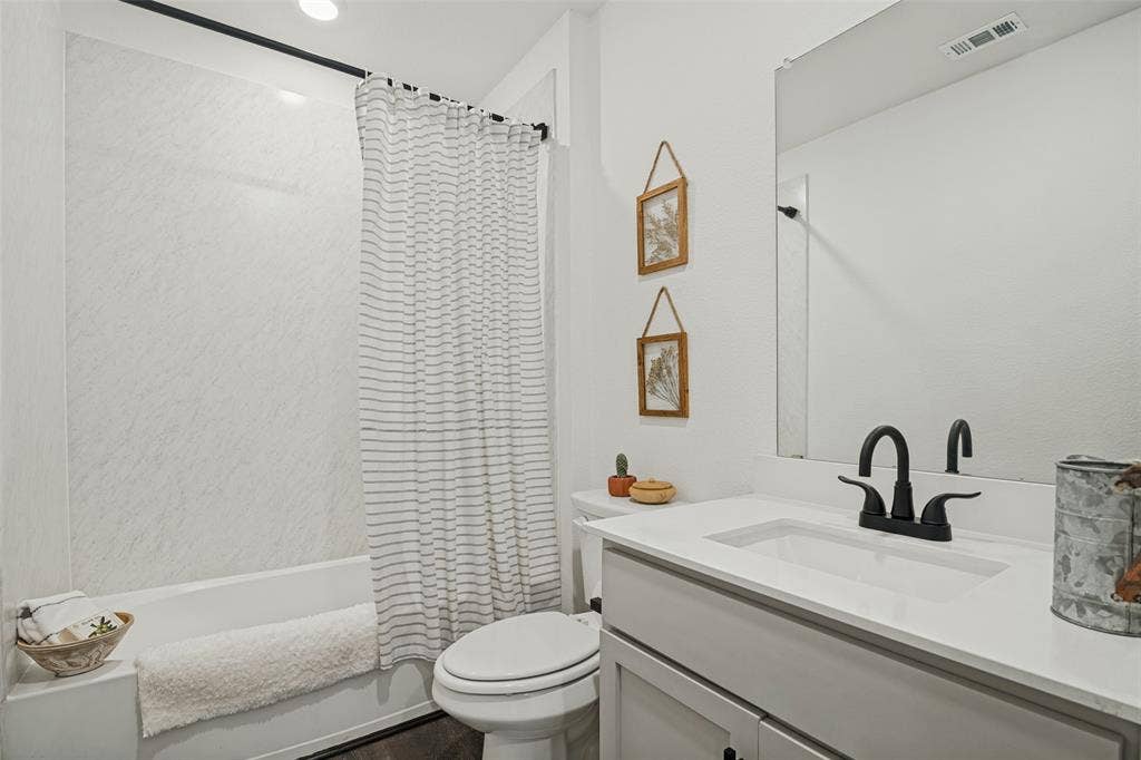 1506 Buckaroo Lane, Josephine, TX 75189 Full bathroom featuring a white vanity with a solid-surface countertop, matte black widespread faucet, large wall-mounted mirror, and a tub-shower combination with light-toned surround panels