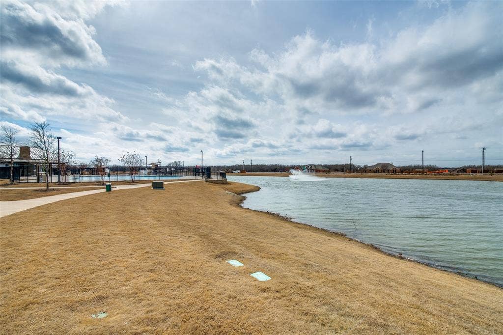 1506 Buckaroo Lane, Josephine, TX 75189 Waterfront property featuring a pond, a concrete walking path, a water fountain, and open lawn space