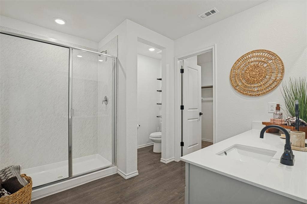 1506 Buckaroo Lane, Josephine, TX 75189 Bathroom featuring a glass-enclosed walk-in shower with solid-surface surround, vanity with stone-style countertop and matte black fixtures, wood-finish flooring, and recessed lighting