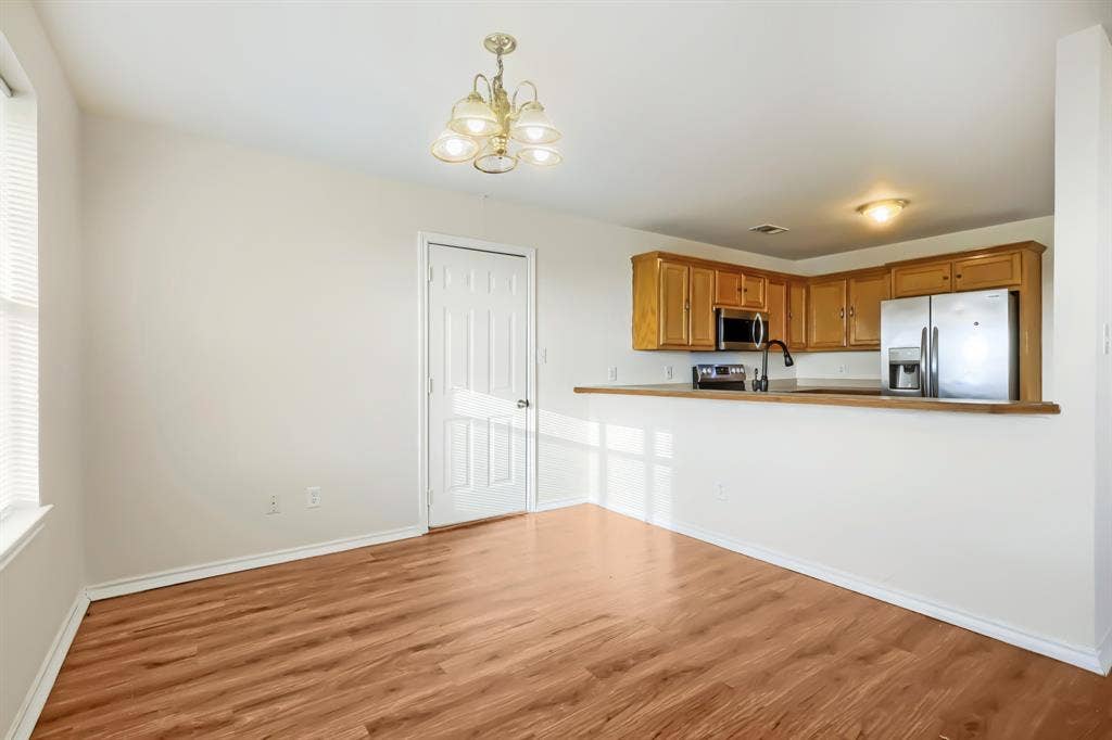 112 Sebastian Lane, Josephine, TX 75173 Dining and eat at bar featuring laminate wood-finish flooring, wood cabinetry, stainless steel kitchen appliances, kitchen pass-through counter, and multi-light chandelier