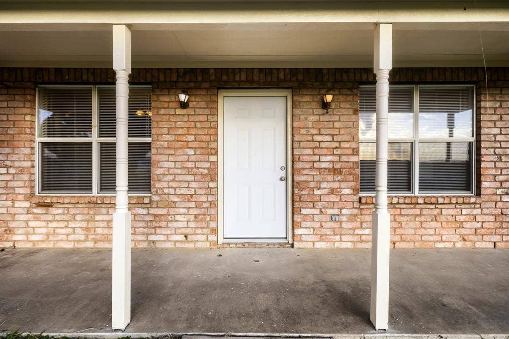 112 Sebastian Lane, Josephine, TX 75173 Covered front porch with concrete flooring, brick exterior wall, dual white support columns, and two wall-mounted light fixtures