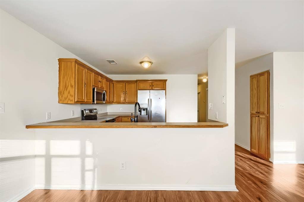 112 Sebastian Lane, Josephine, TX 75173 Kitchen featuring wood cabinetry, stainless steel appliances, breakfast bar, and laminate wood-finish flooring throughout living spaces.