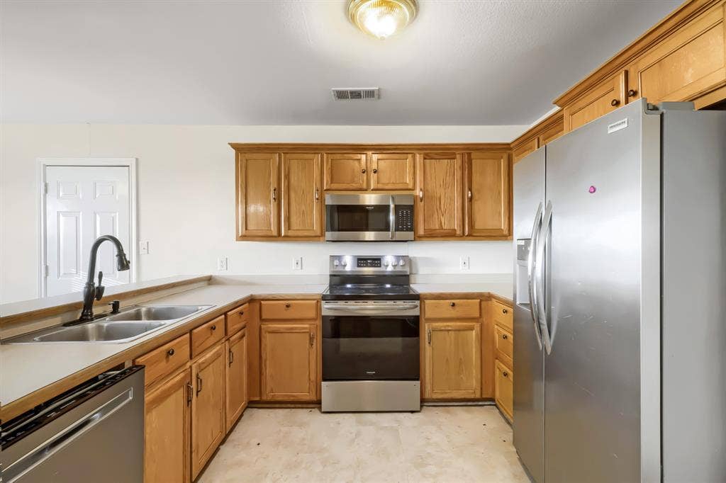 112 Sebastian Lane, Josephine, TX 75173 Kitchen featuring wood cabinetry, stainless steel appliances, dual-basin sink with matte black faucet, and solid-surface countertops