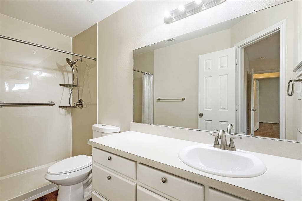 112 Sebastian Lane, Josephine, TX 75173 Bathroom featuring a white vanity with a countertop basin, large wall-mounted mirror, brushed metal hardware, and a tub-shower combination with an integrated shelving unit and grab bar