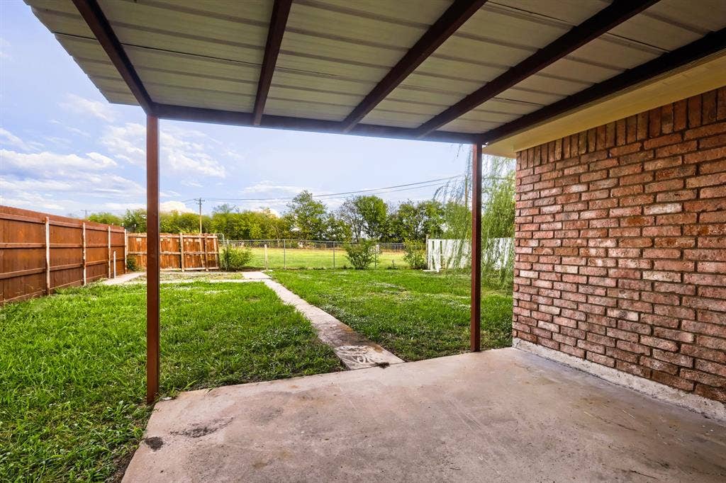 112 Sebastian Lane, Josephine, TX 75173 Covered concrete patio with metal roof framing, red brick exterior wall, and wood-panel privacy fencing enclosing a lawn area