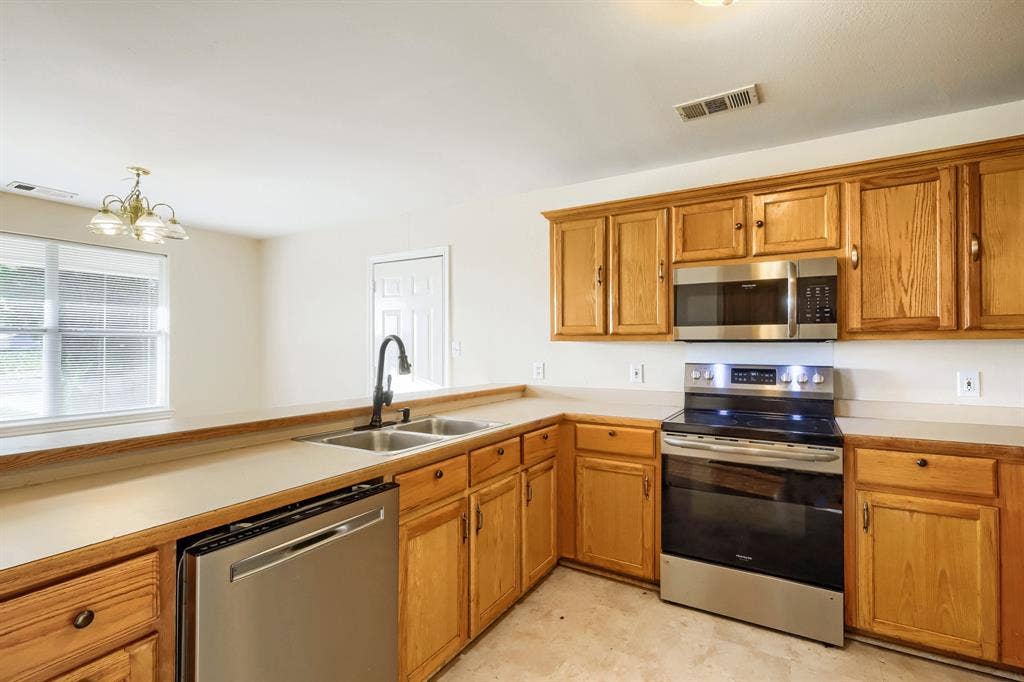 112 Sebastian Lane, Josephine, TX 75173 Kitchen featuring wood cabinetry, stainless steel appliances, a dual-basin sink with a matte black faucet, and solid-surface countertops