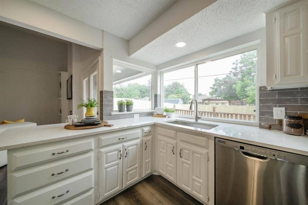 1903 Arvada Drive, Richardson, TX 75081 Kitchen featuring white cabinetry, quartz countertops, gray tile backsplash, stainless steel sink with high-arc faucet, and stainless steel dishwasher