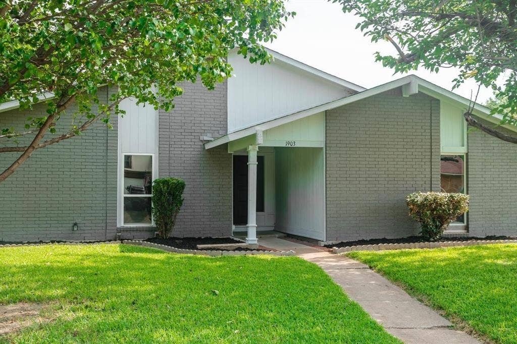 1903 Arvada Drive, Richardson, TX 75081 Exterior featuring grey brick facade, vertical wood-panel siding, covered entryway with a column, and a concrete walkway
