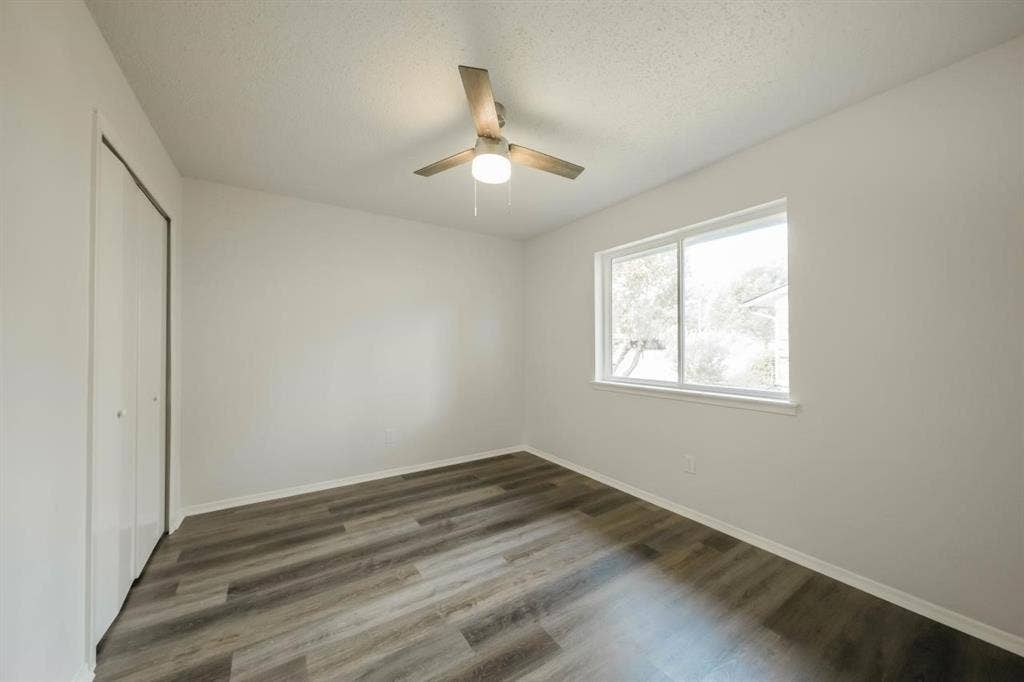 1903 Arvada Drive, Richardson, TX 75081 Neutral-toned interior featuring wood-finish flooring, sliding door closet, single-pane window, and integrated ceiling fan with lighting
