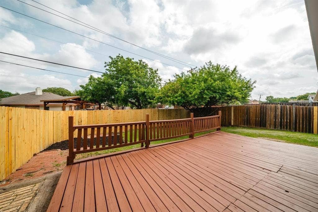 1903 Arvada Drive, Richardson, TX 75081 Elevated wooden deck with horizontal railing, enclosed by a full-height wood privacy fence and featuring a brick-paved ground section