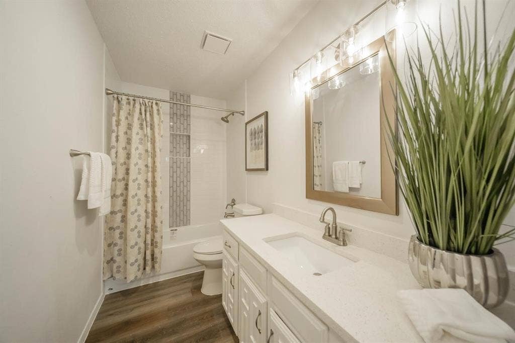 1903 Arvada Drive, Richardson, TX 75081 Bathroom featuring a white vanity with a quartz countertop, an integrated rectangular sink, wood-finish flooring, and a tub-shower combination with decorative vertical tile inlay