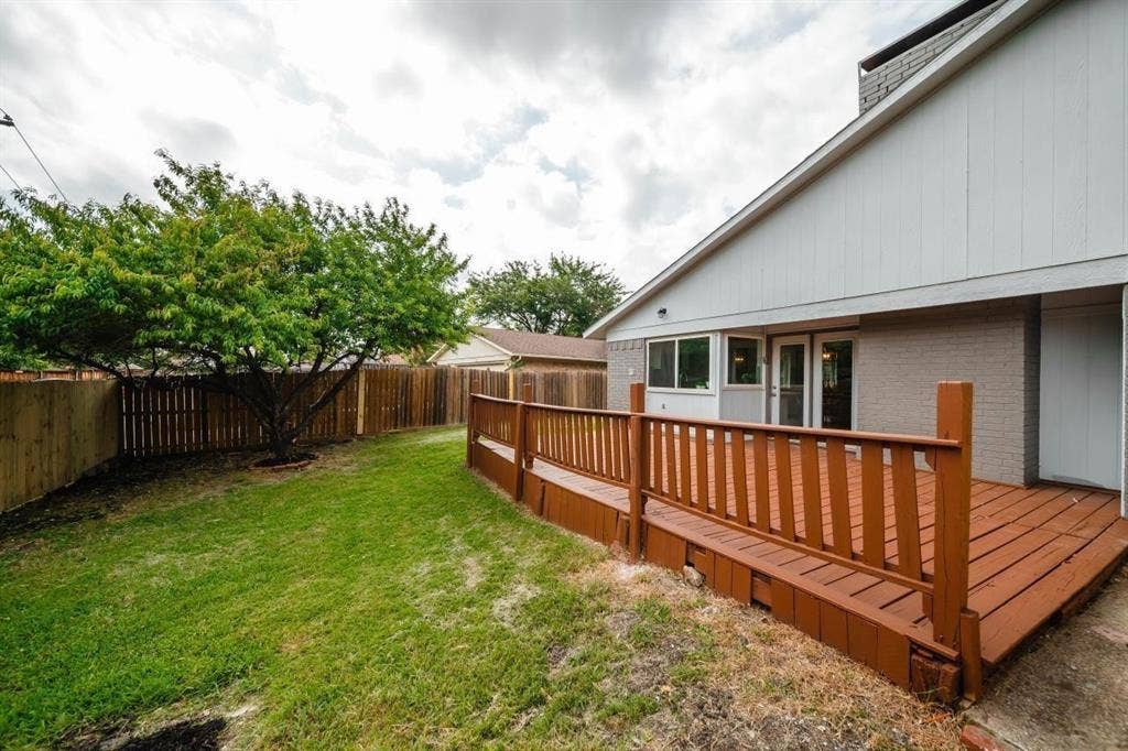1903 Arvada Drive, Richardson, TX 75081 Backyard featuring a raised wood deck, perimeter wood fencing, a mature tree, and a grass lawn