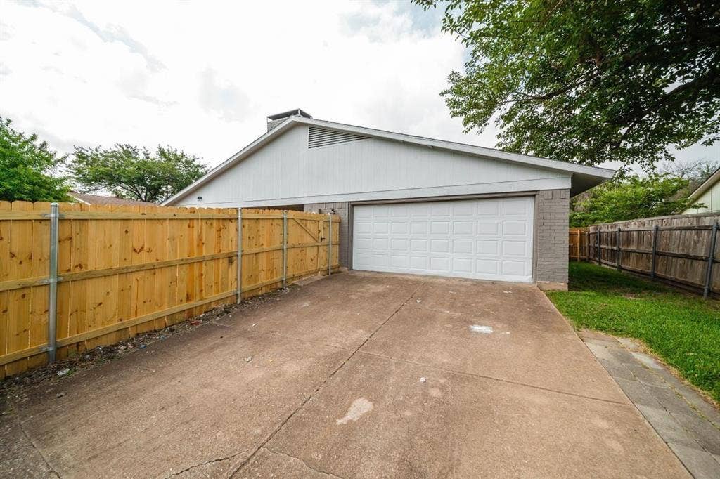 1903 Arvada Drive, Richardson, TX 75081 Attached two-car garage featuring a white sectional door, concrete driveway, and full wood privacy fencing