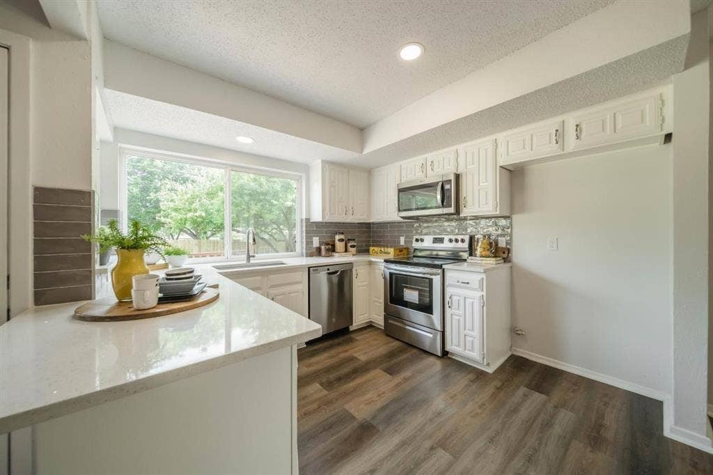 1903 Arvada Drive, Richardson, TX 75081 Kitchen featuring white cabinetry, stainless steel appliances, wood-finish flooring, quartz-style countertops, and a tile backsplash