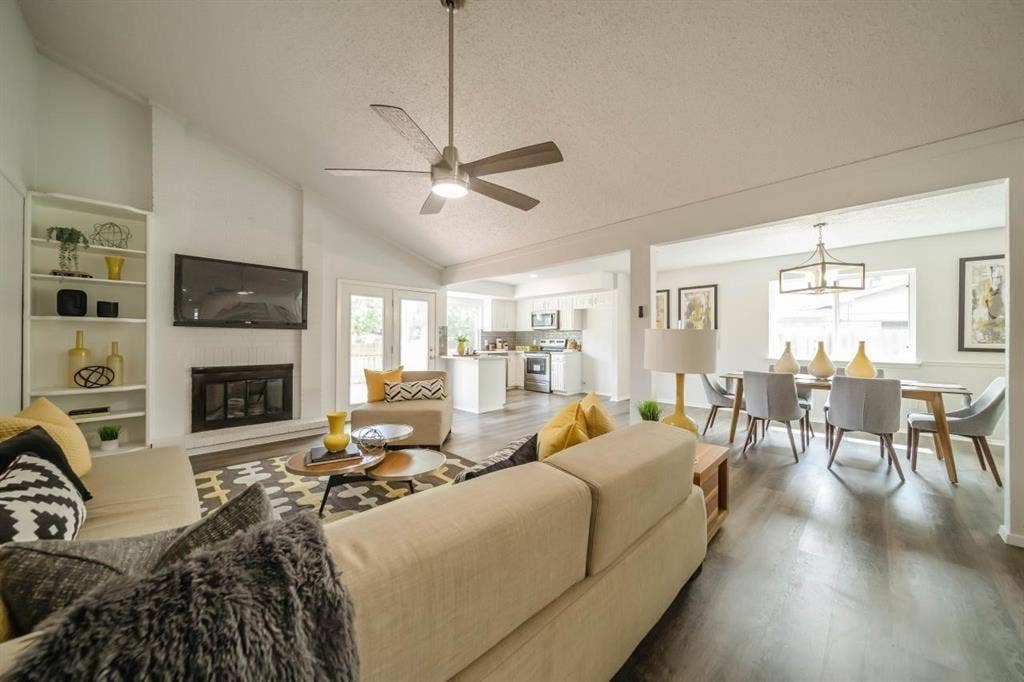 1903 Arvada Drive, Richardson, TX 75081 Vaulted ceiling with a central brushed-nickel ceiling fan, wood-finish flooring, built-in shelving, and a gas fireplace with a black surround