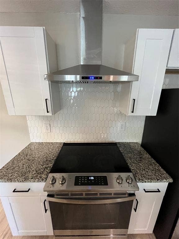 600 Royal Crest Drive, Richardson, TX 75081 Stainless steel range, chimney-style range hood, white shaker-style cabinetry, stone-finish countertops, and white elongated hexagonal tile backsplash