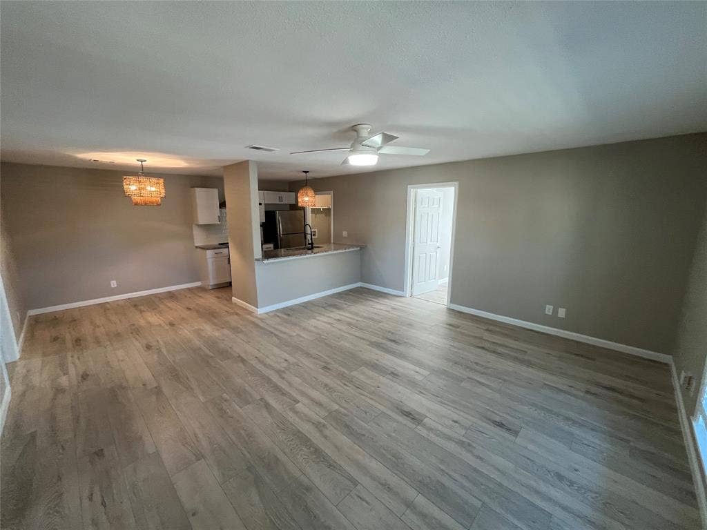600 Royal Crest Drive, Richardson, TX 75081 Open-concept space featuring wood-finish flooring, a kitchen peninsula with stone-surface countertop, modern pendant lighting, and a ceiling fan