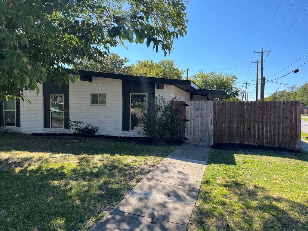 600 Royal Crest Drive, Richardson, TX 75081 Mid-century modern exterior featuring painted brick facade, flat roofline with exposed rafter tails, vertical trim accents, and a wood privacy fence