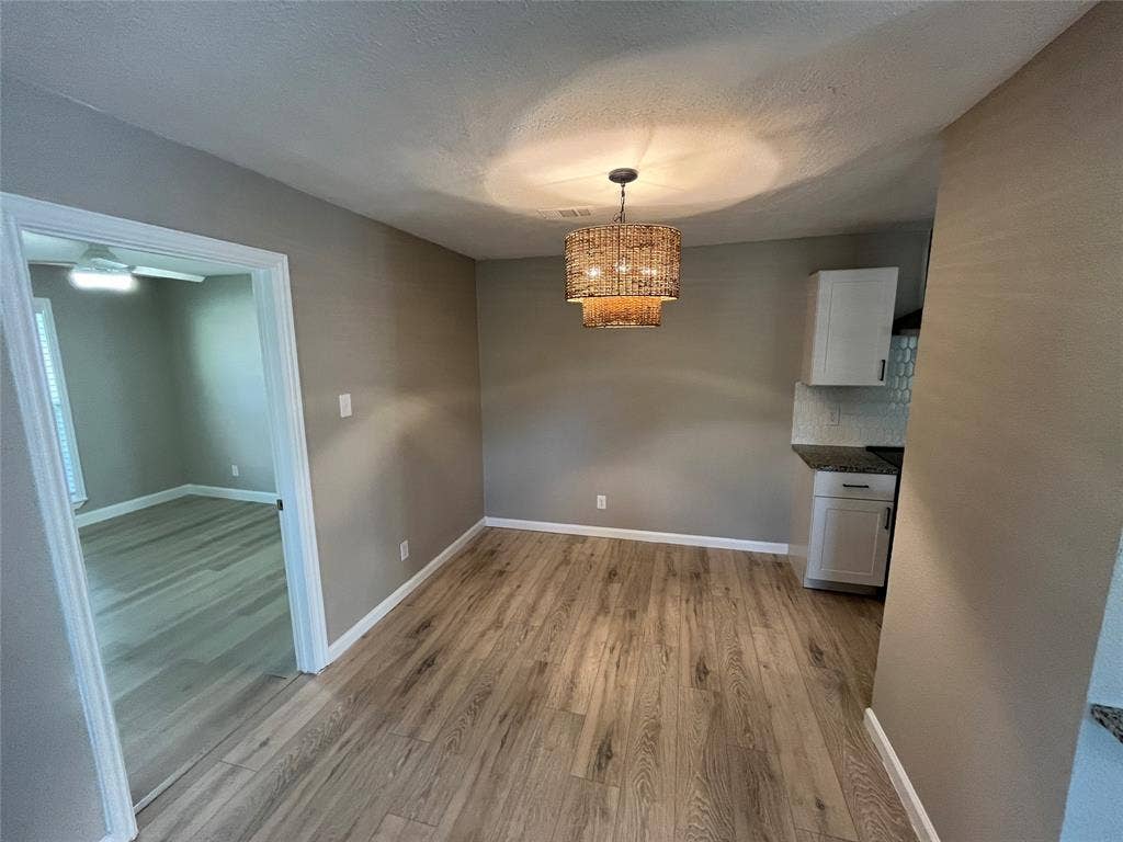 600 Royal Crest Drive, Richardson, TX 75081 Wood-finish flooring, textured drum pendant lighting, white cabinetry, and a geometric tiled backsplash